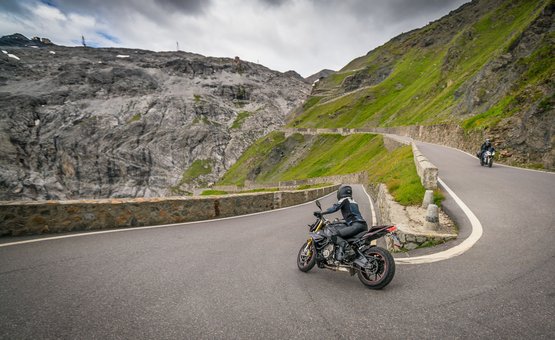 Moto Fun Anna *** © Moppetfoto.de Motorcyclists riding on winding mountain road with rocky cliffs and cloudy sky