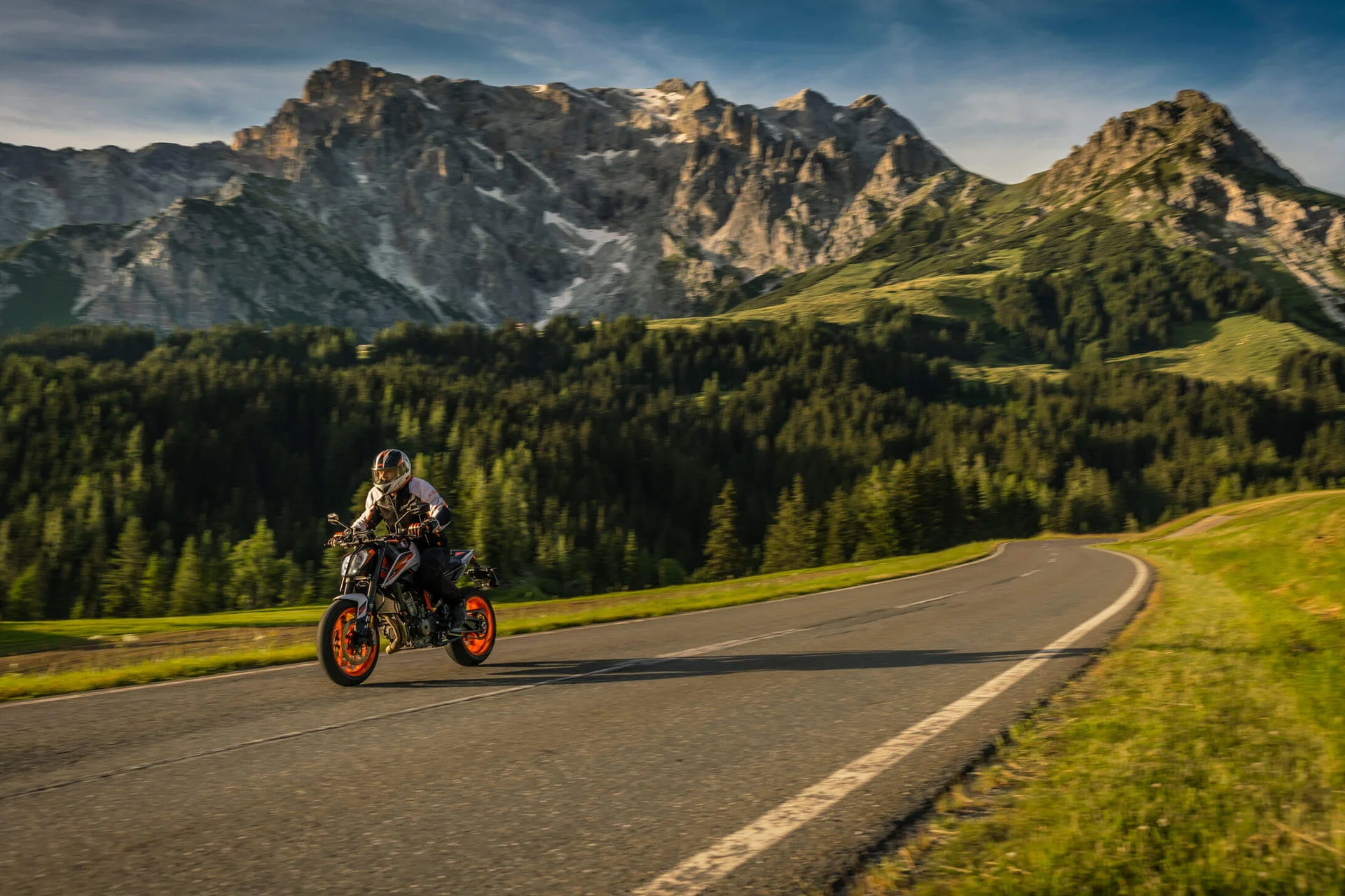 Motorradurlaub © Moppetfoto.de Motorradfahrer auf Bergstraße mit bewaldeten Hügeln und steilen Gipfeln im Hintergrund